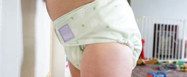 A close up picture of a toddler wearing a green reusable nappy from Bambino Mio's Miosolo Supreme range. In the background you can see toys on the living room floor.