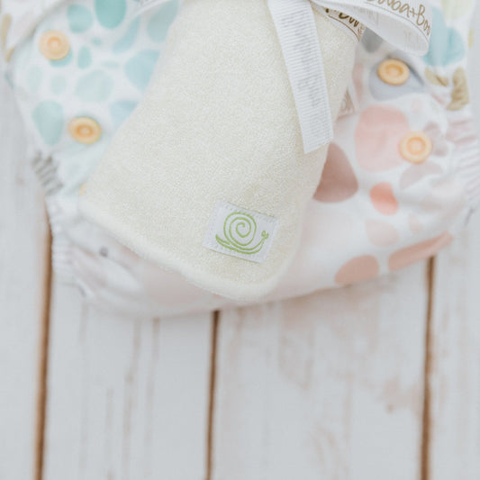 Five wipes rolled up and sat on top of a cloth nappy.